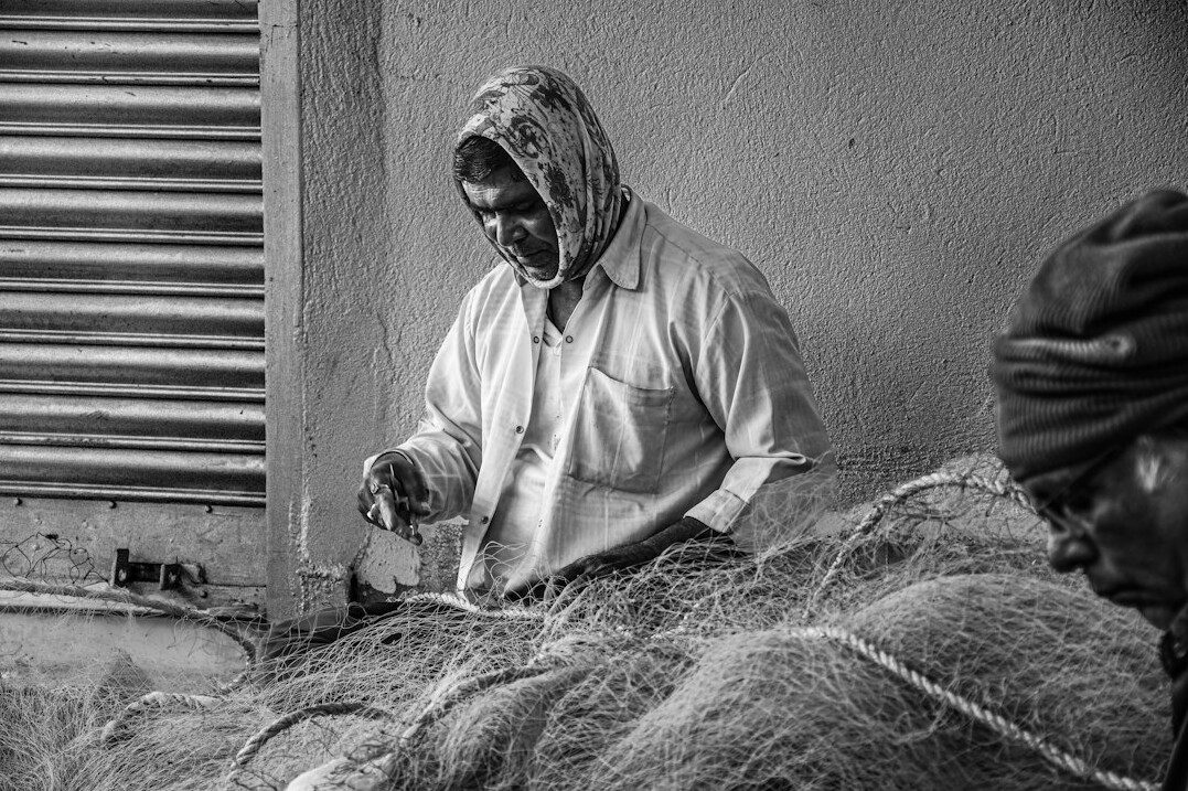 Elderly Danish fisherman mending fishing nets at the harbor